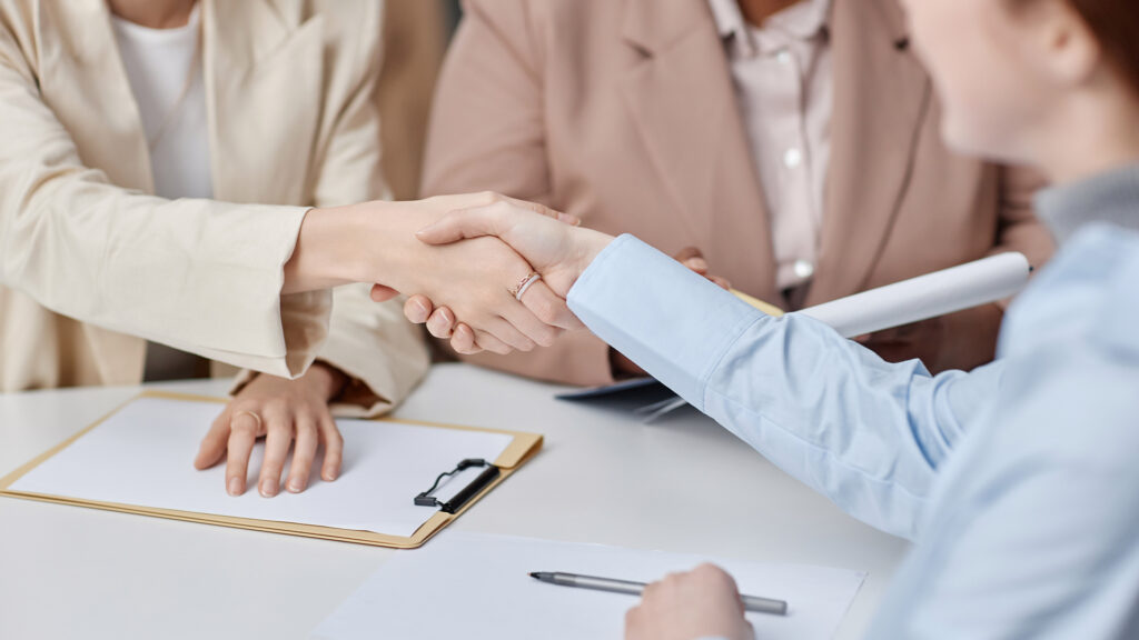 Close up shot of handshake between unrecognizable female company employees while sitting at office table