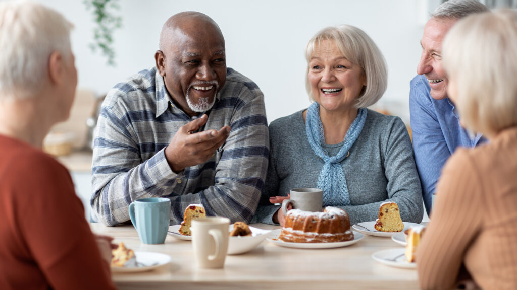 International group of positive elderly people drinking tea with cake